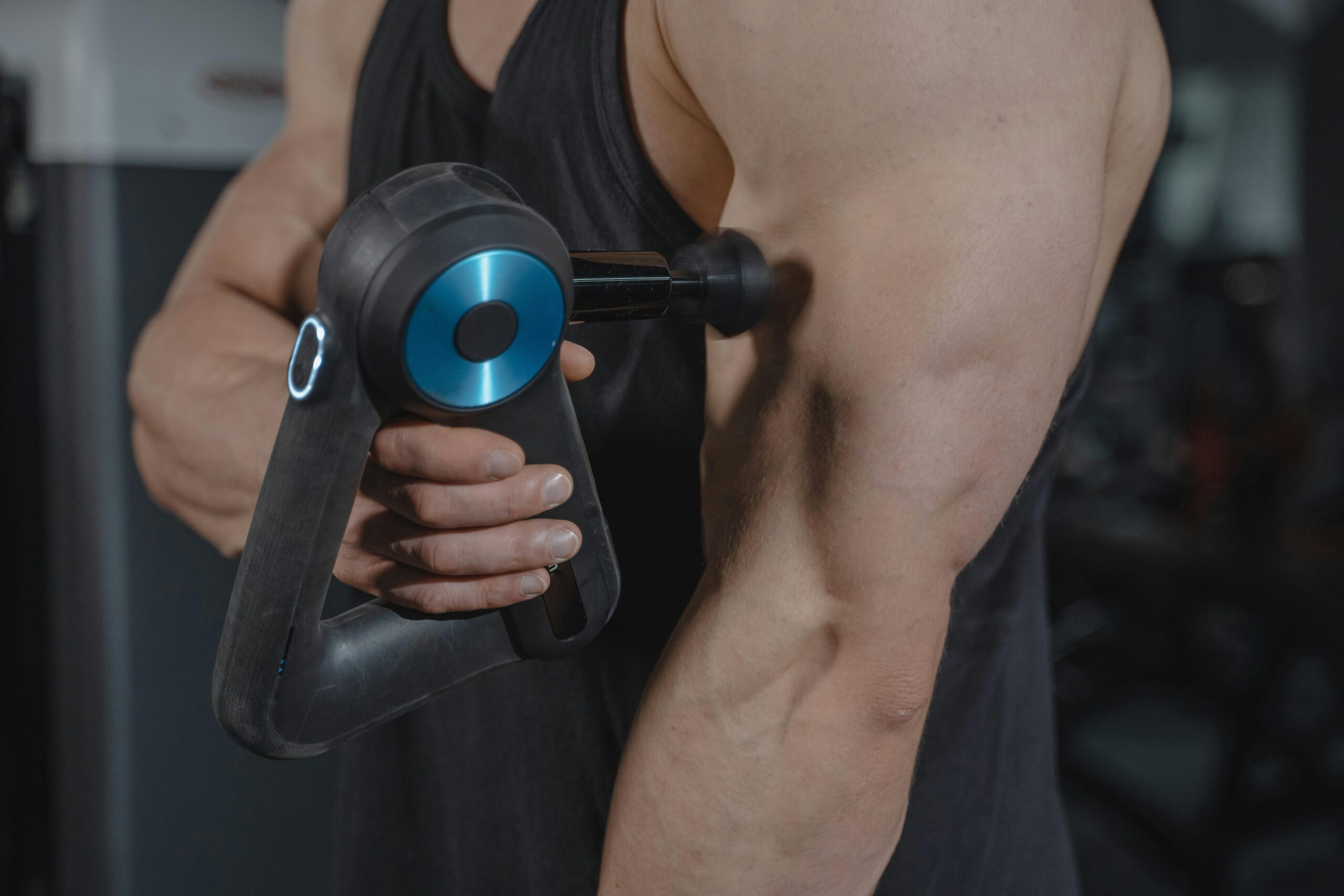 Close-up of a man using a massage gun for muscle relaxation on his arm.